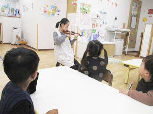 保育園でバイオリンを弾く先生の写真