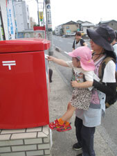 保育園児が先生に抱っこされてポストに手紙を投函する様子