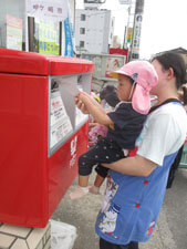 保育園児が先生に抱っこされてポストに手紙を投函する様子