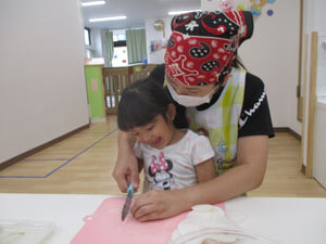 先生と大根を切る保育園児