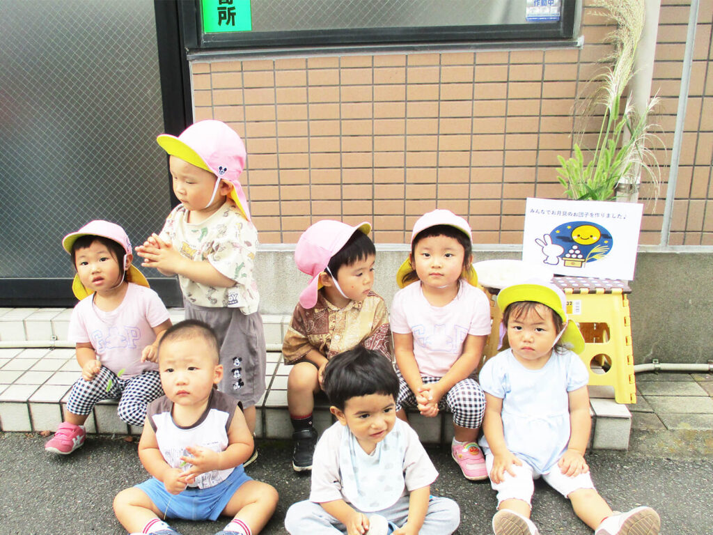 手作りお月見団子とススキの前で集合写真を撮る保育園児