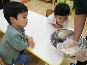 小麦粉をこねる保育園の先生を見る保育園児の様子