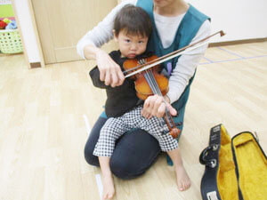 バイオリンを弾く保育園児と手伝う先生