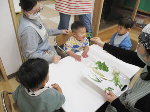 春の七草を見せる先生と保育園児の様子